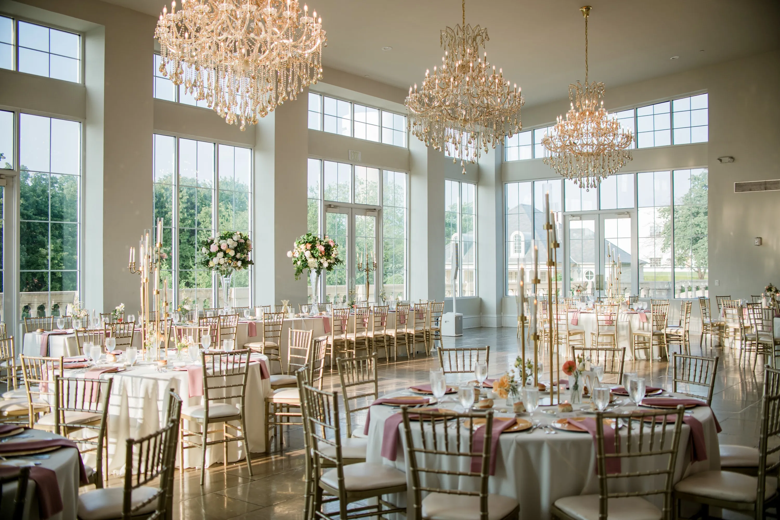 A sunlit ballroom set for a wedding reception, with crystal chandeliers and blush linens